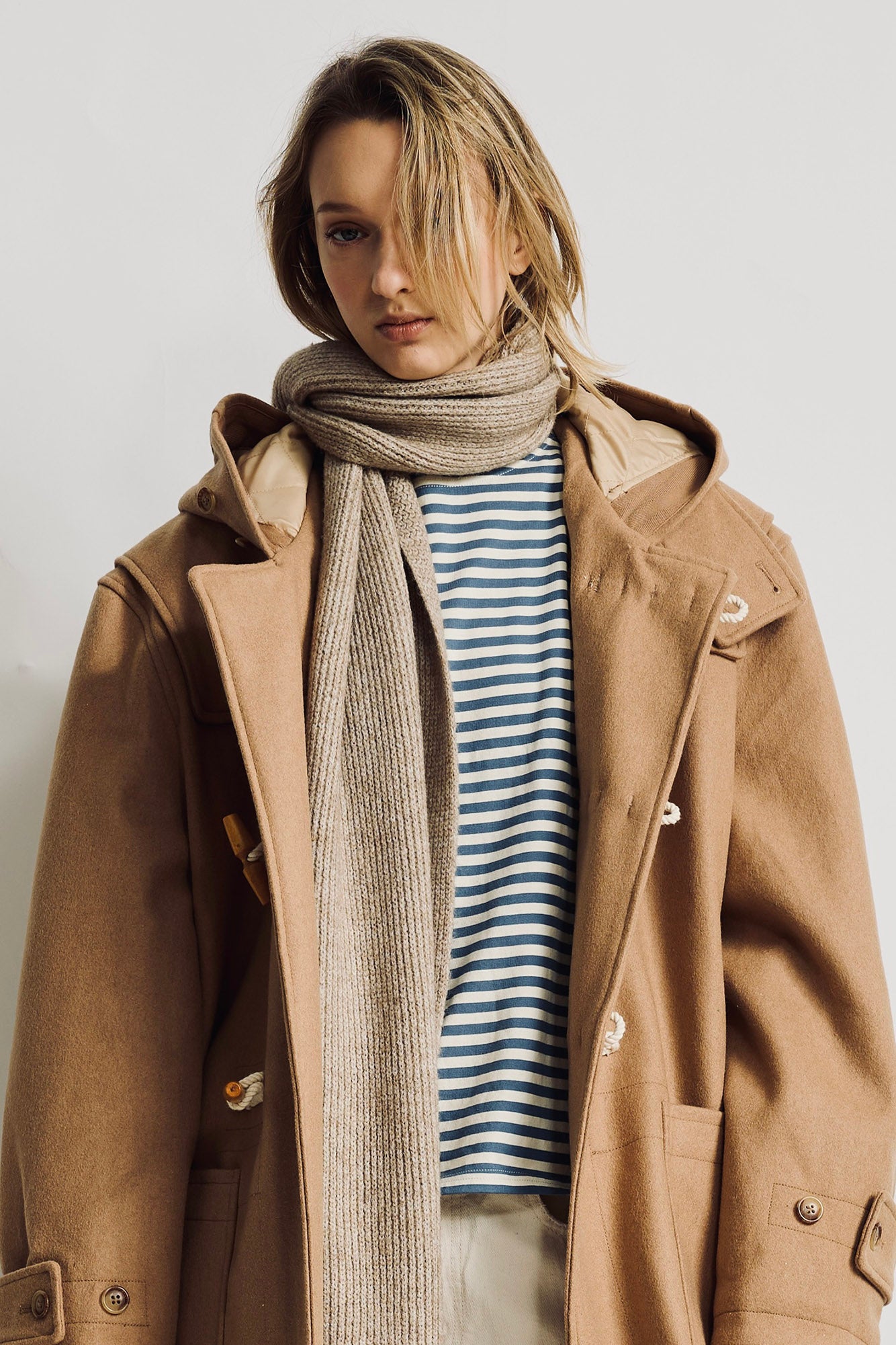Blue and white striped short-sleeve tee worn under a tan coat and gray scarf.