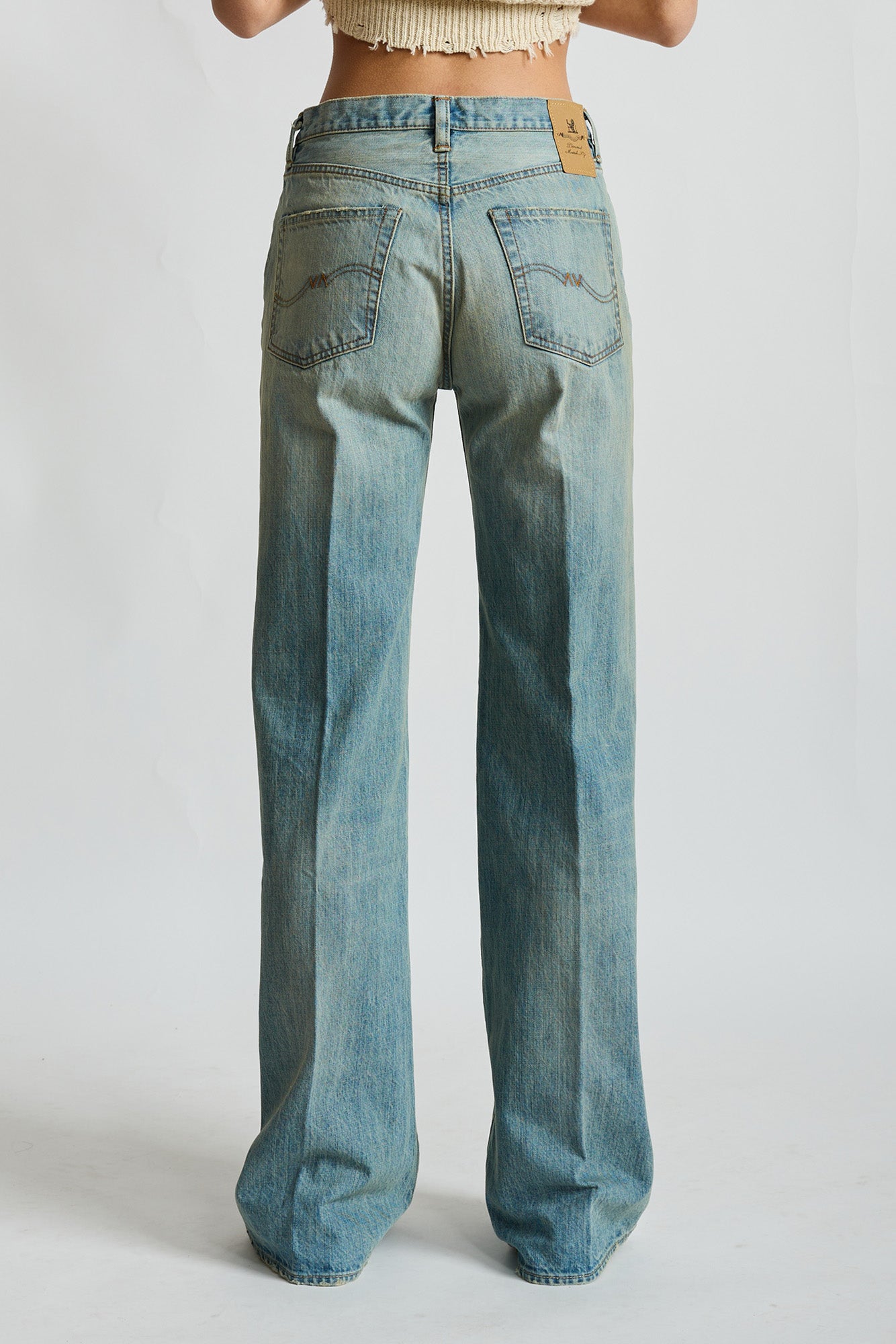 Light indigo wide-leg jeans with back patch pockets and tan leather label, worn high-waisted.