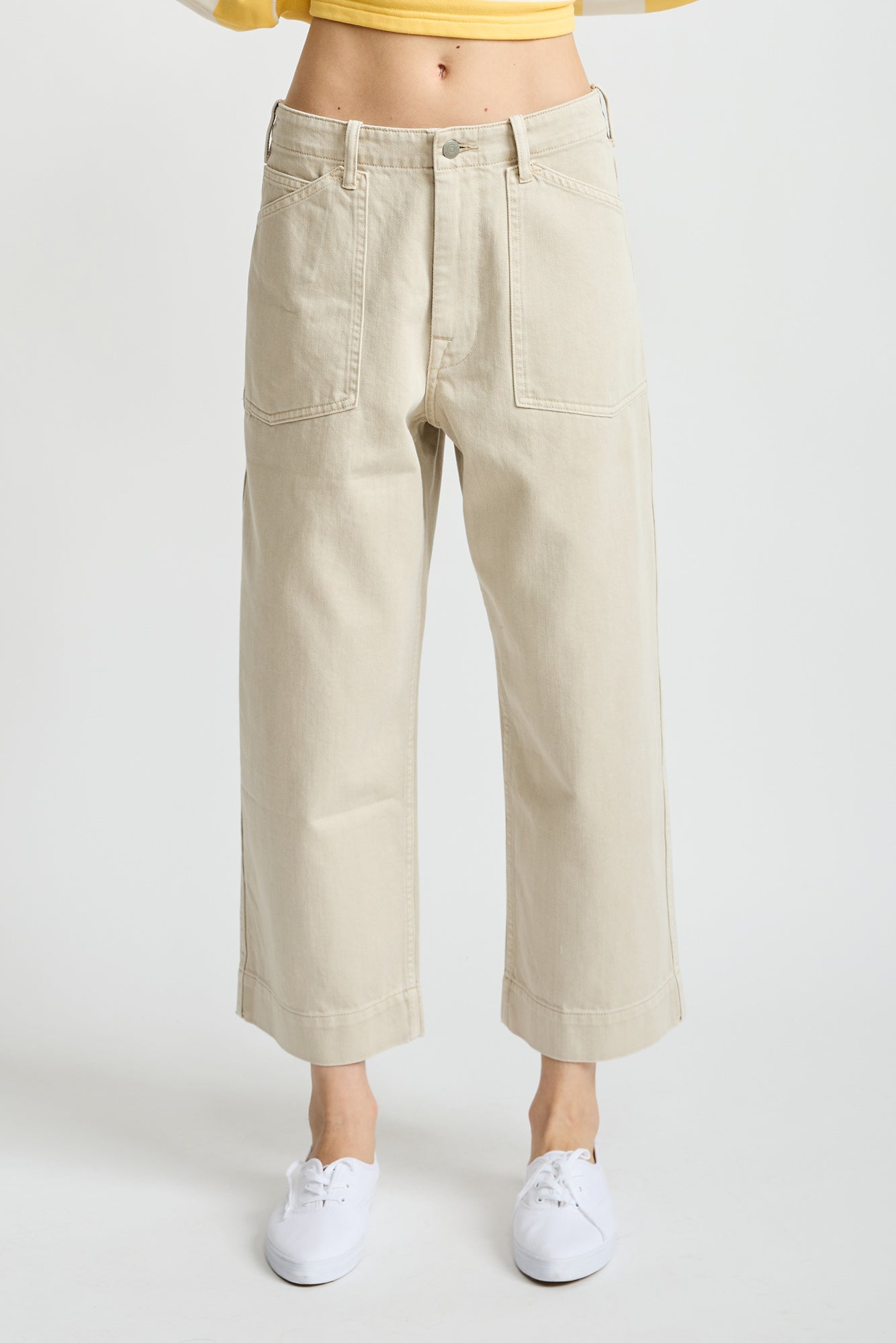 Light brown work pants with large front pockets and cropped leg length, worn with white sneakers.