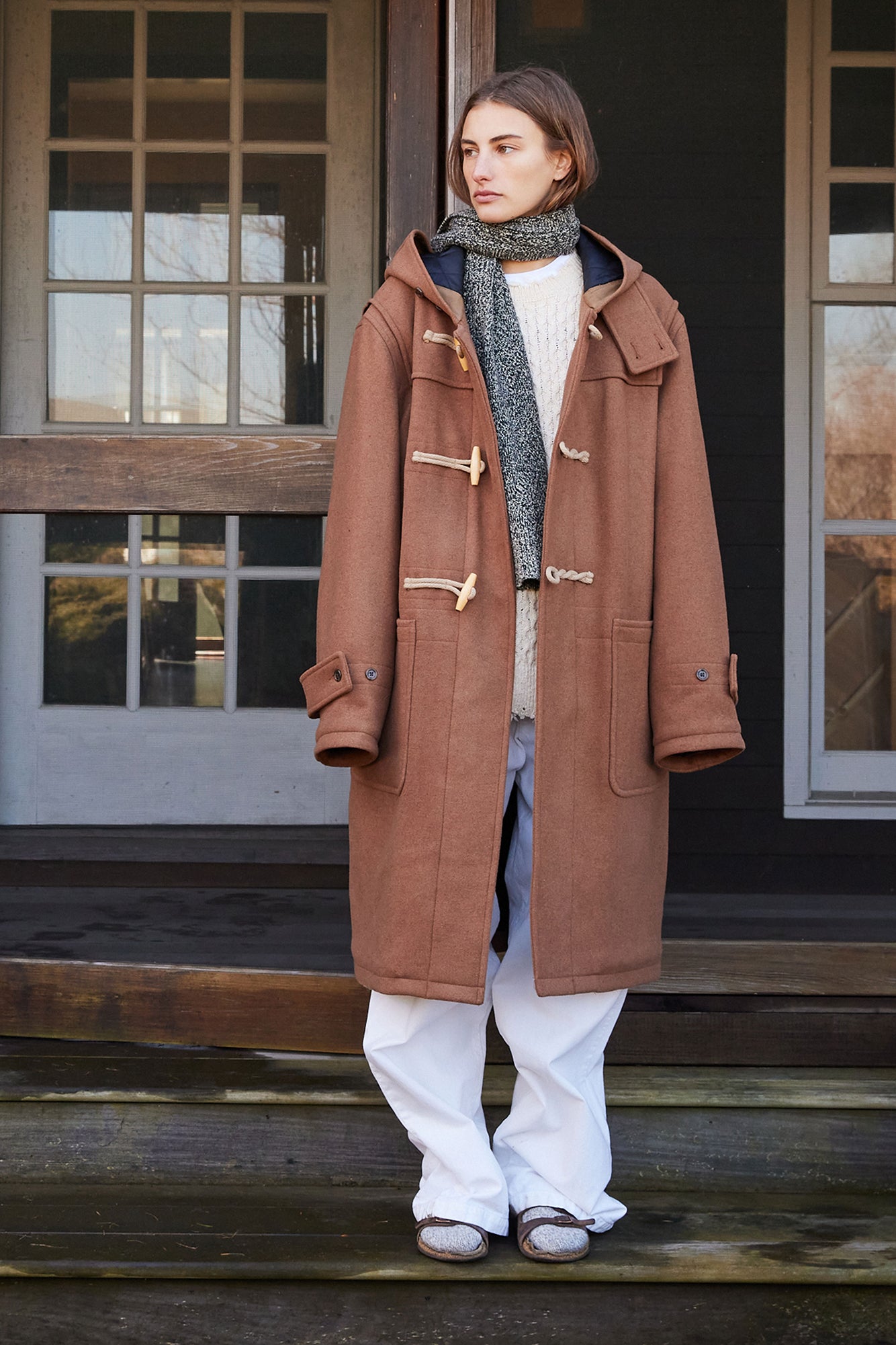Woman wearing a brown coat standing on wooden steps.